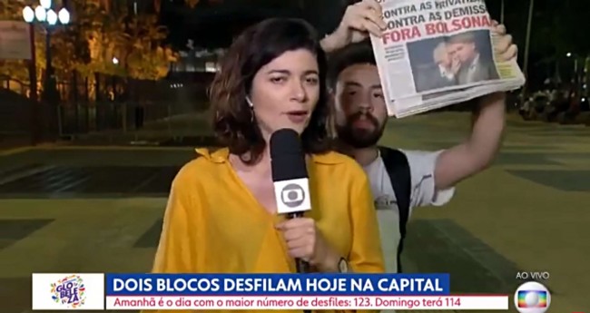 Repórter da Globo e rapaz com jornal estampando fora Bolsonaro