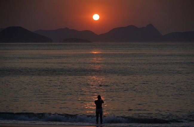 Homem entra na água para registrar o nascer do sol, no dia que pode ser o mais quente do ano no Rio — Foto: Marcos Serra Lima/G1